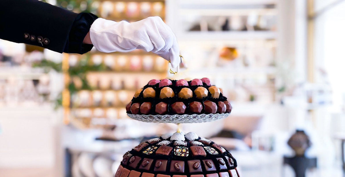 A tower of Makaw chocolate bonbons being finished by hand with a white glove