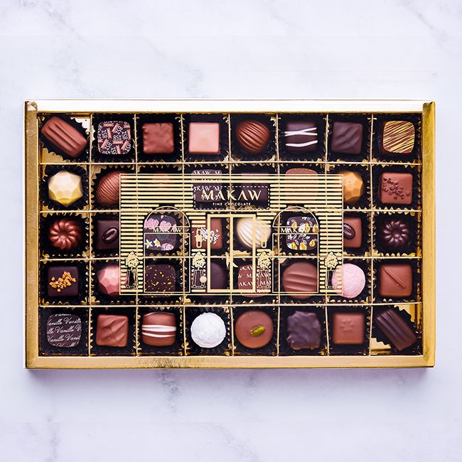 Open gold MAKAW box of 40 assorted chocolate bonbons with the boutique card